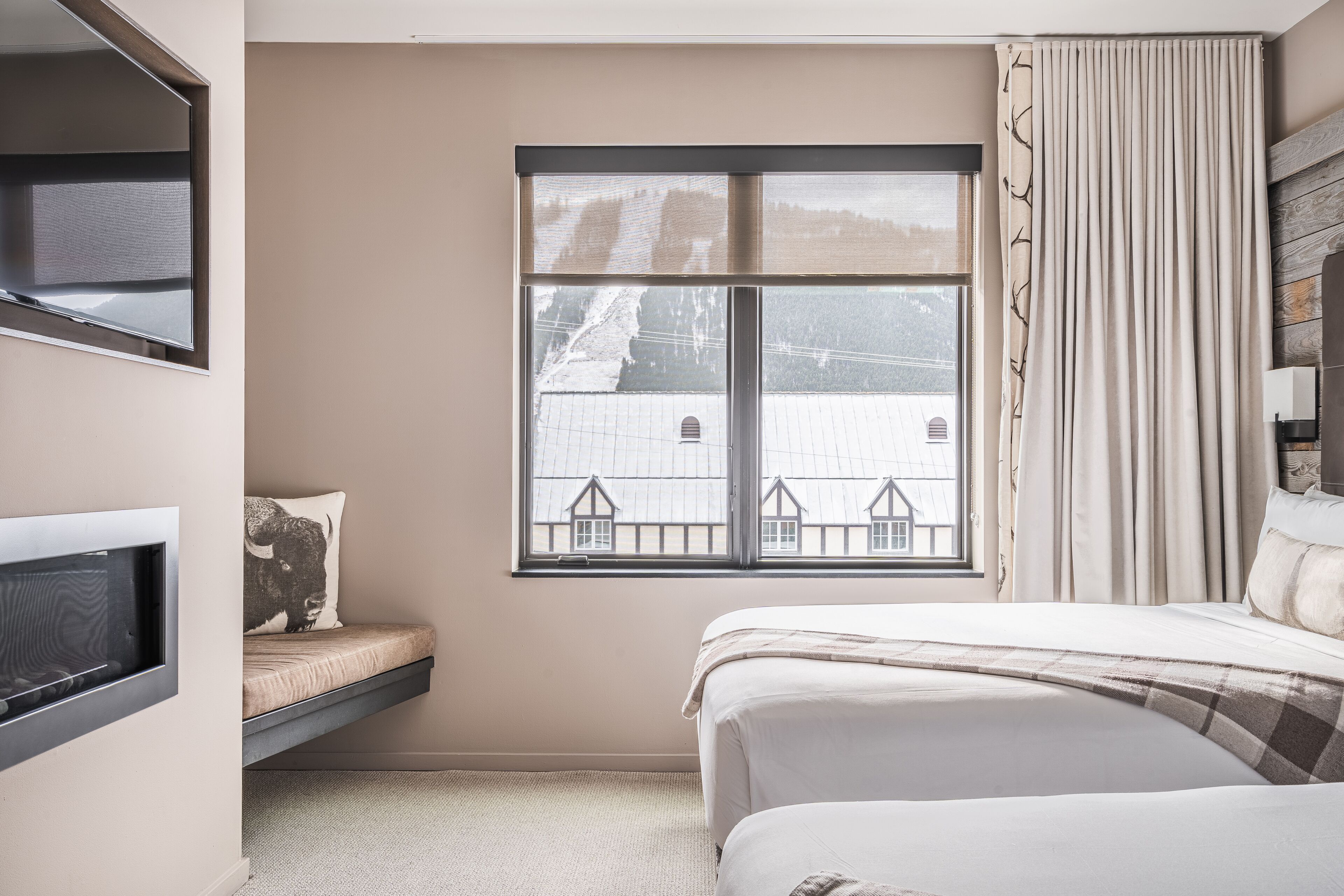 Quarto com cama, janela com vista para uma casa, televisão embutida e mesa de cabeceira.