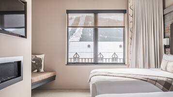 Quarto com cama, janela com vista para uma casa, televisão embutida e mesa de cabeceira.