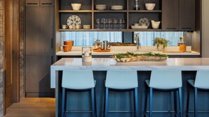 A modern kitchen with a central island, bar stools, and built-in shelves with dishes and glasses.