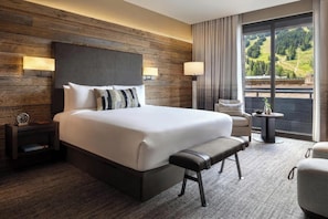 A modern hotel room with a large bed, bedside lamps, a bench, a small table, and a view of a green landscape. - Hotel Jackson (Jackson)