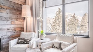 A room with two white armchairs, a small round table with a potted plant, and a view of trees through a large window. - Hotel Jackson (Jackson)