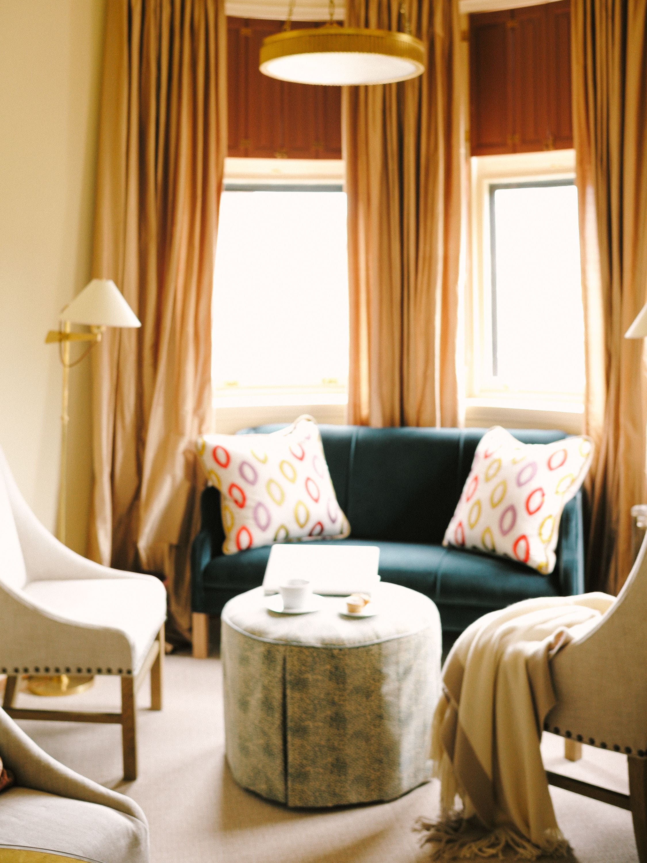 A cozy living room with a green sofa, two patterned pillows, a round coffee table, and a lamp.