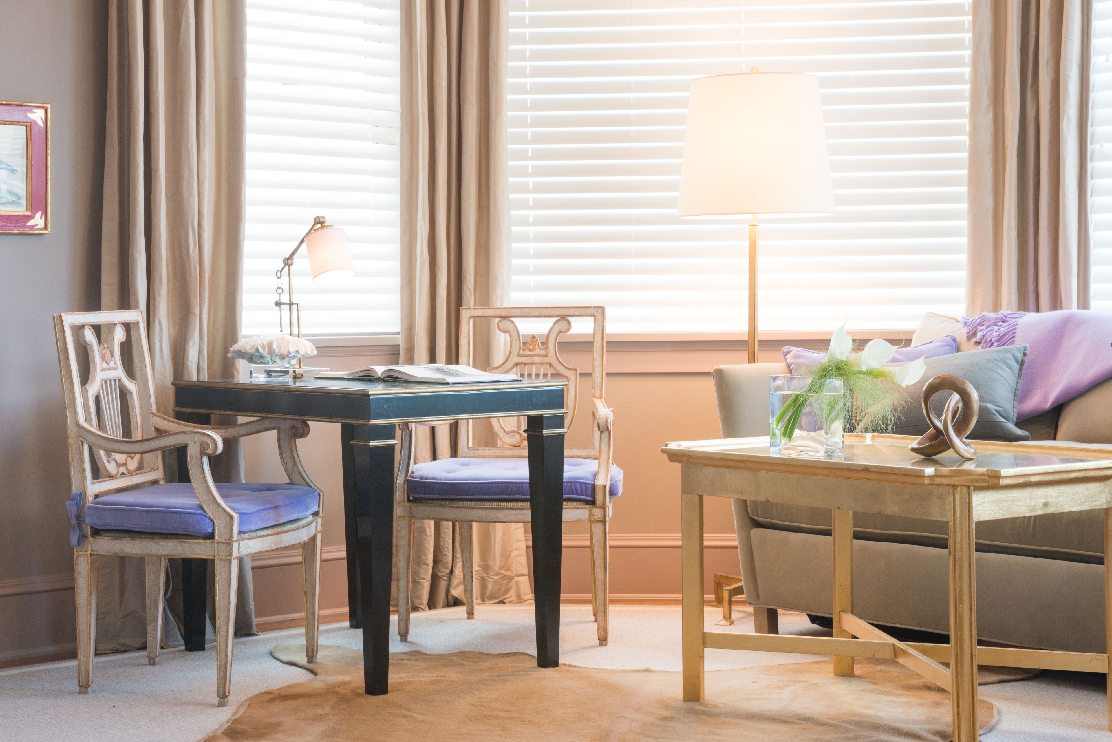 A room with a wooden desk, two chairs, a sofa, and a lamp.