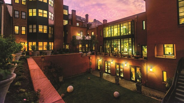 A courtyard with a brick building, potted plants, and a well-lit outdoor area. - The Ivy Hotel (Baltimore)