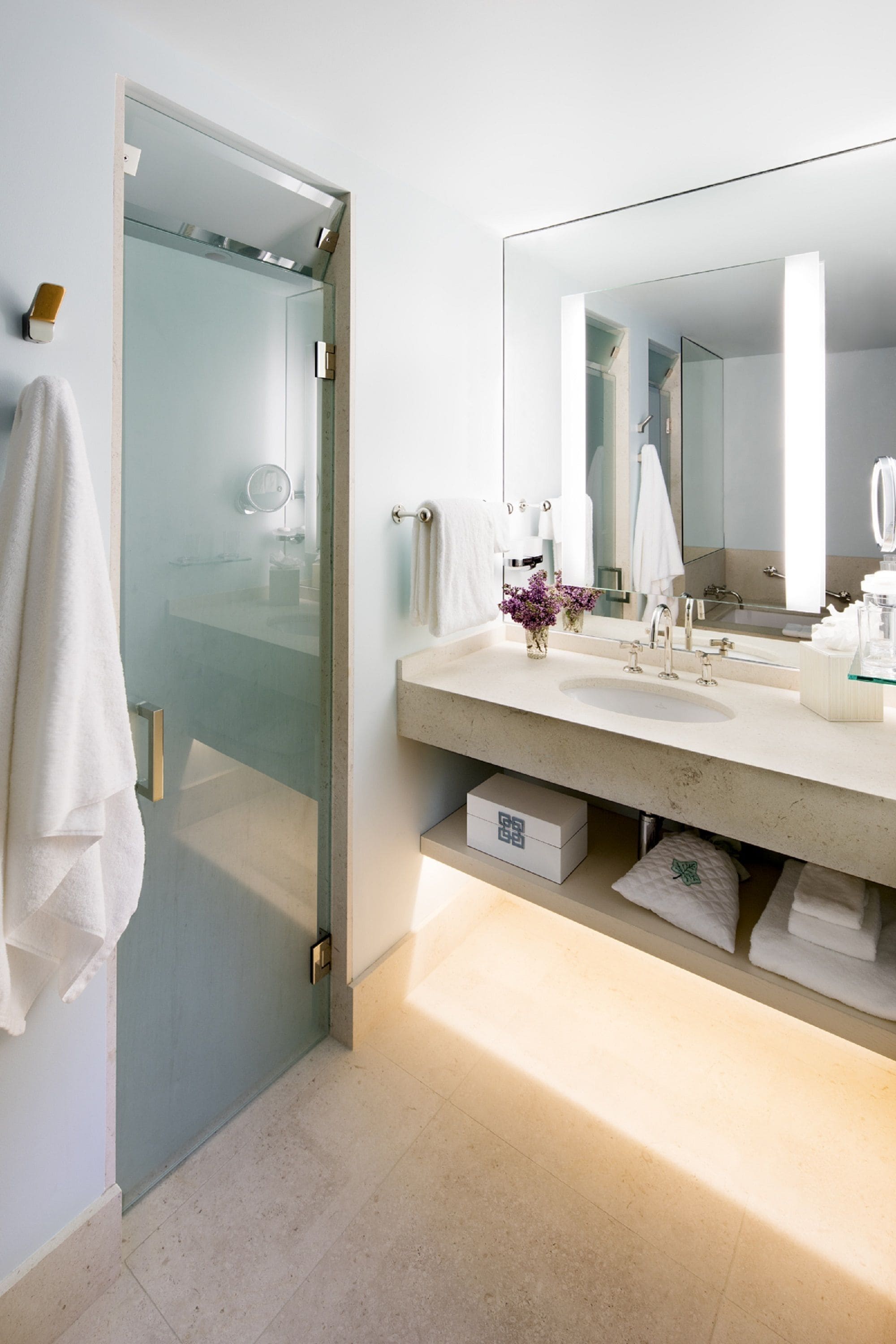 Un baño moderno con mampara de vidrio, un espejo grande y encimera color beige.