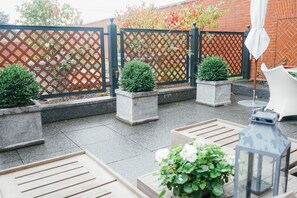 Een terras met een bakstenen muur, een lattenhek en planten in potten.