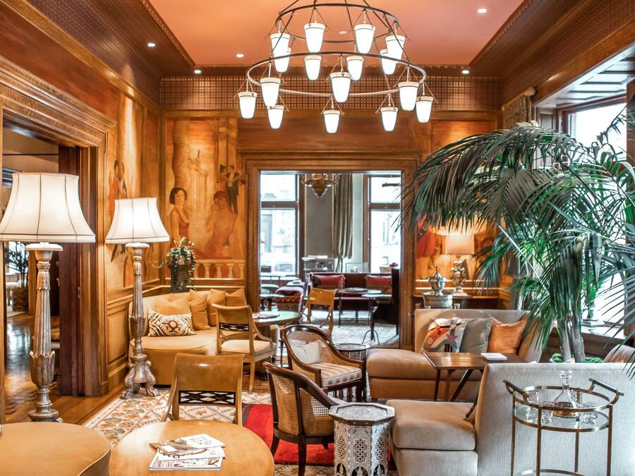 A luxurious lobby with a high ceiling, ornate chandeliers, plush seating, and a large plant.
