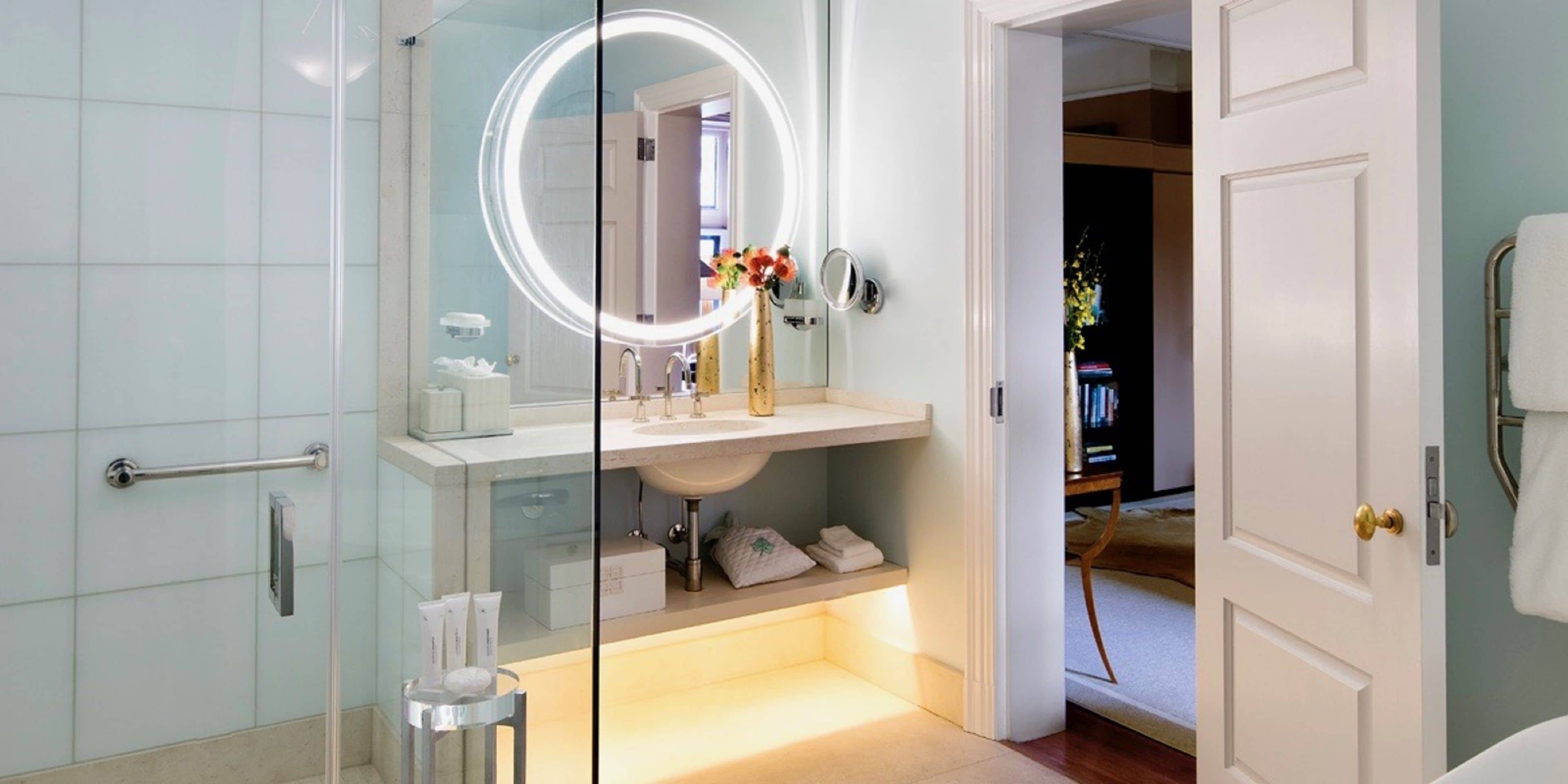 Une salle de bain moderne avec une douche à parois de verre, un meuble-lavabo doté d’un miroir rond et un lavabo blanc.
