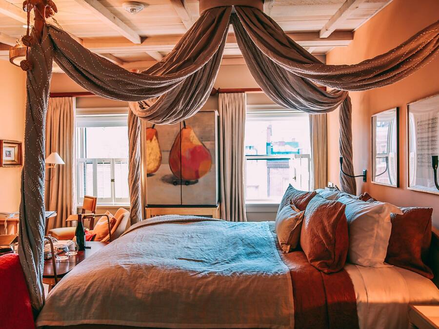 A bedroom with a canopy bed, a desk with a chair, and a large window with curtains.