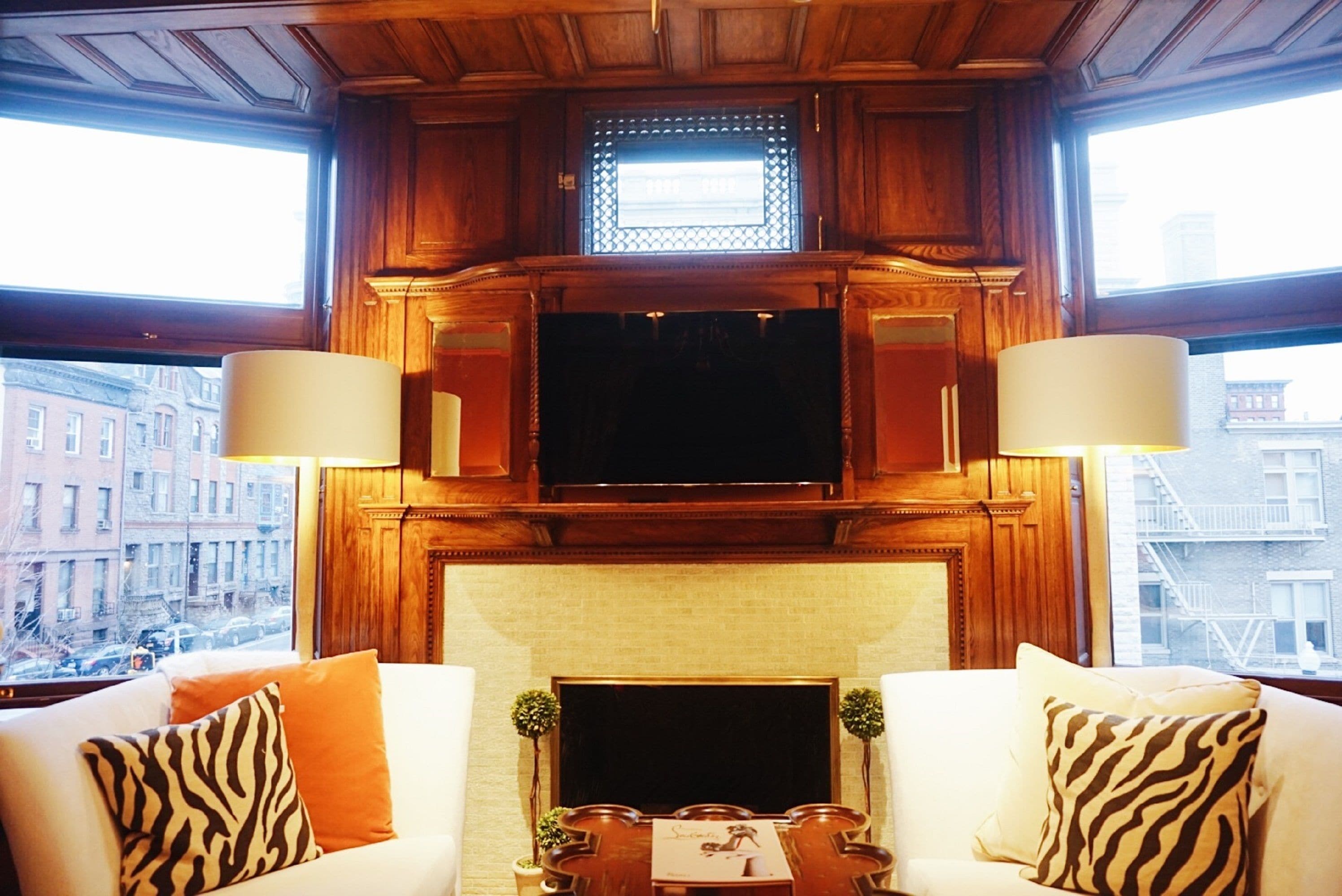A cozy living room with a fireplace, wooden paneling, and a television mounted above it. There are two couches with patterned cushions and a small table with a decorative item.
