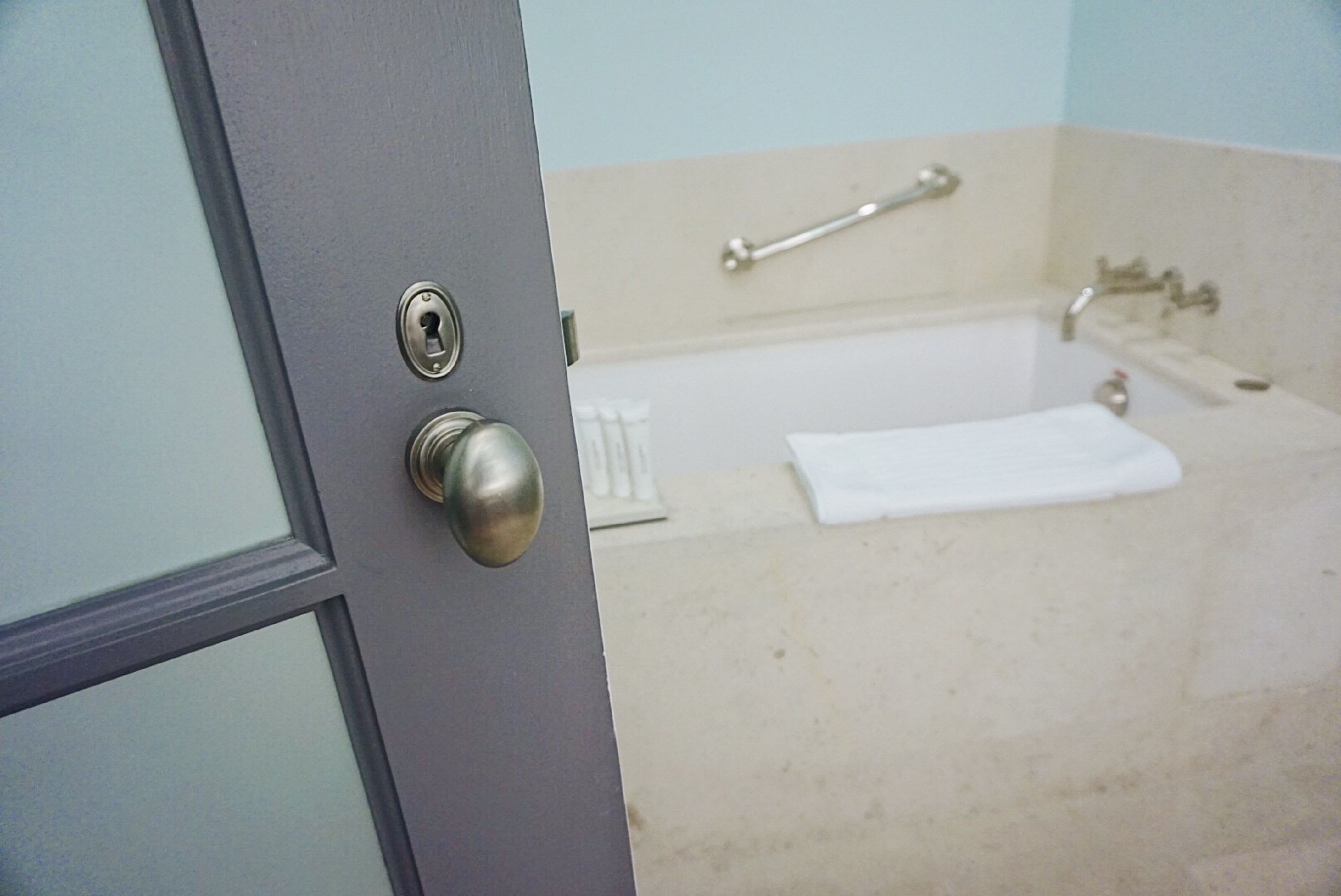 A bathroom with a bathtub, a towel, and a door with a lock.
