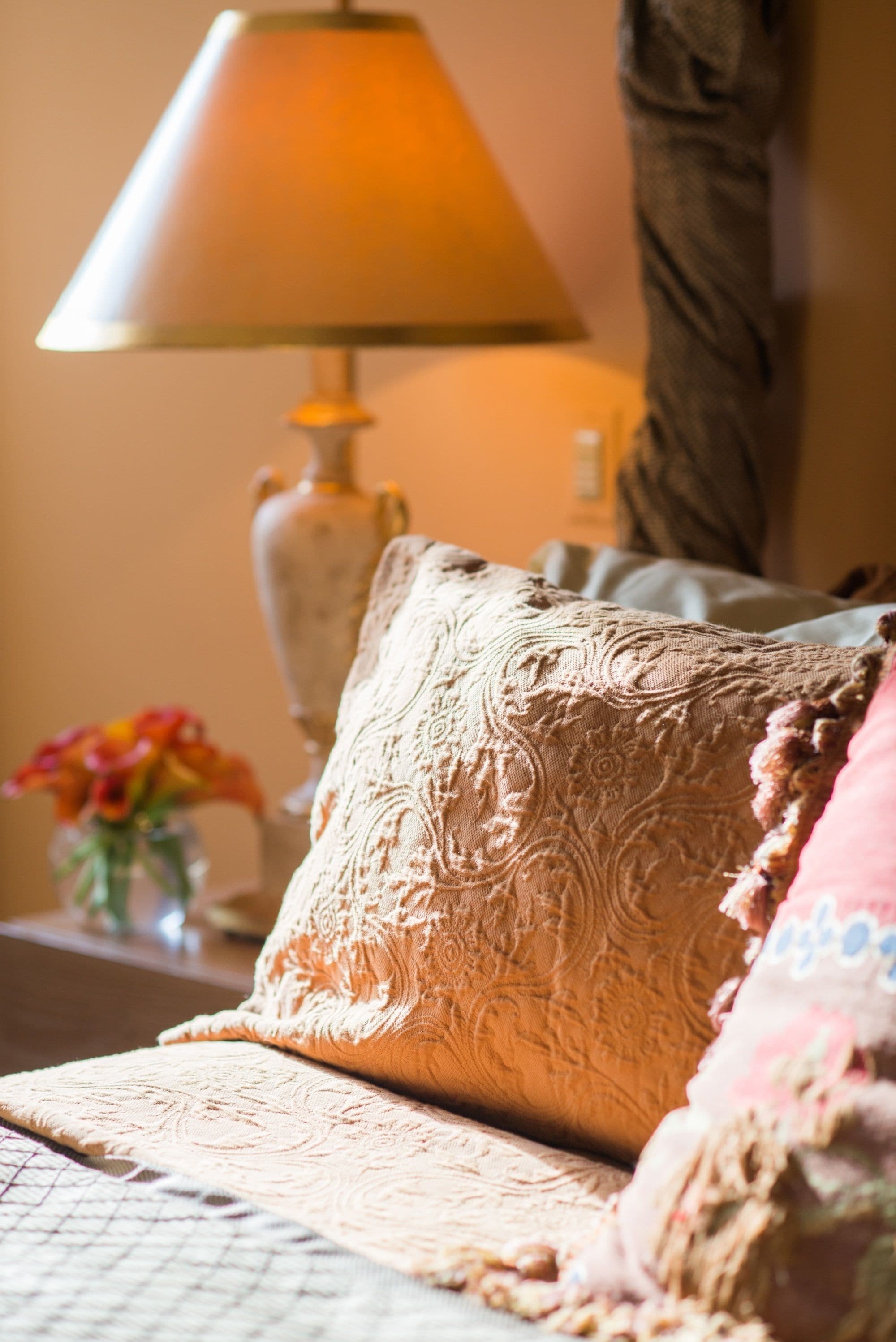 Ein Sofa mit einem gemusterten Kissen, eine Vase mit Blumen und eine Lampe im Hintergrund.