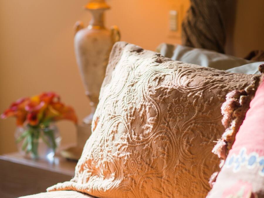 Ein Sofa mit einem gemusterten Kissen, eine Vase mit Blumen und eine Lampe im Hintergrund.