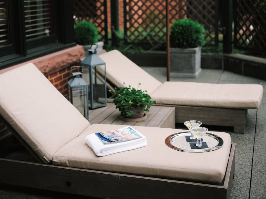 A patio with two lounge chairs, a white umbrella, and a small table with a magazine and a glass.