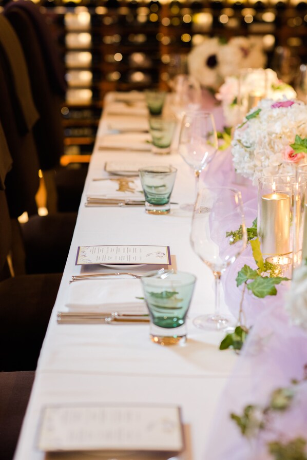 Une longue table à manger, dressée avec de la verrerie, des menus et des bougies, évoquant une ambiance de repas formel.