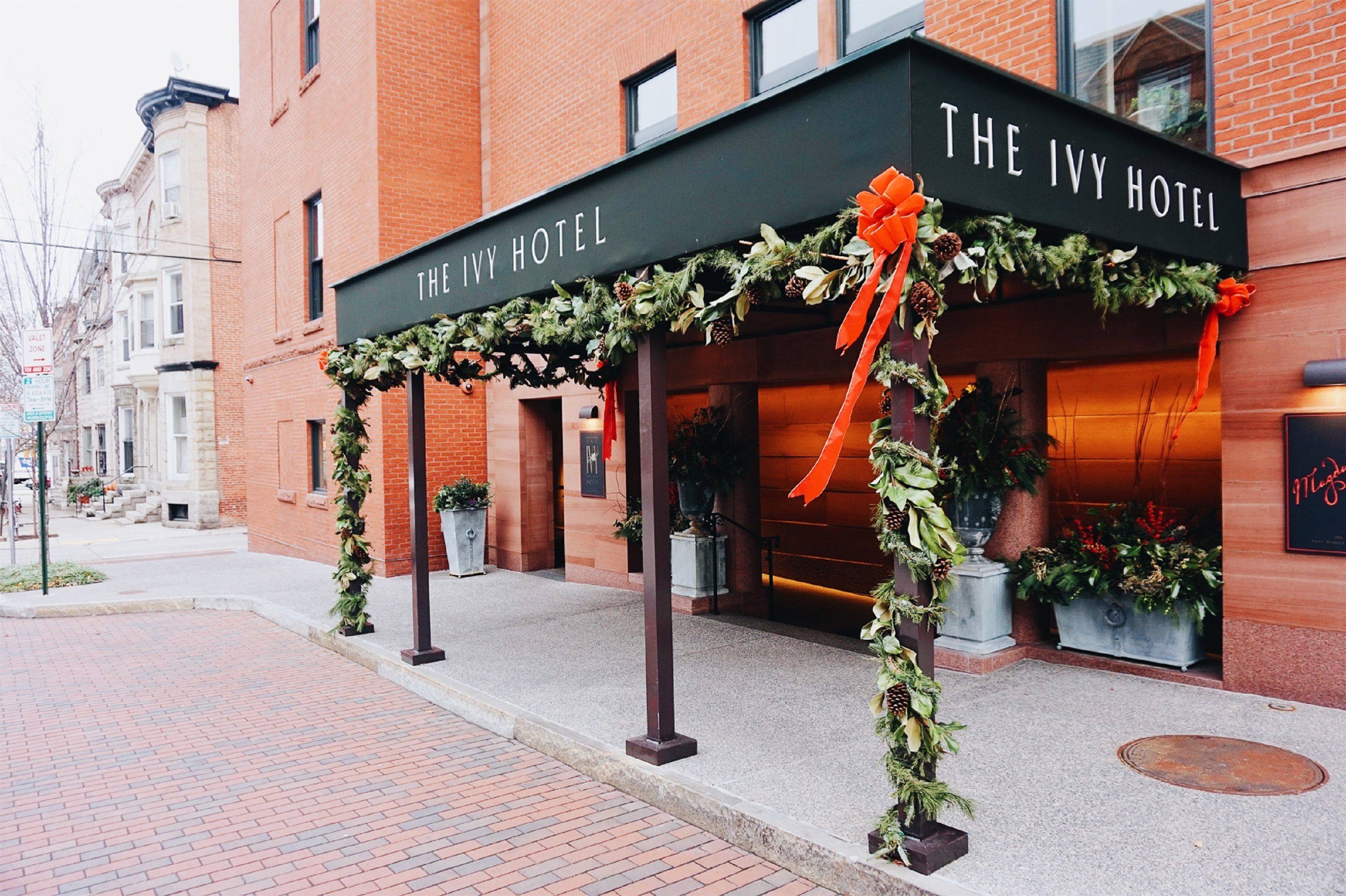 L’hôtel Ivy, avec sa façade en briques, son auvent noir et ses décorations festives, notamment des guirlandes de verdure et un grand nœud orange.