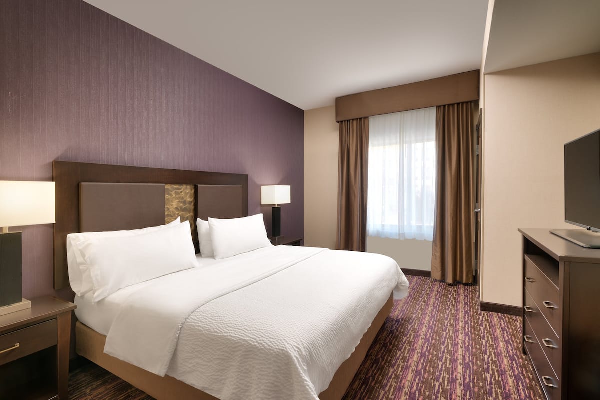 A hotel room with a large bed, a desk with a lamp, a television, and a window with curtains.