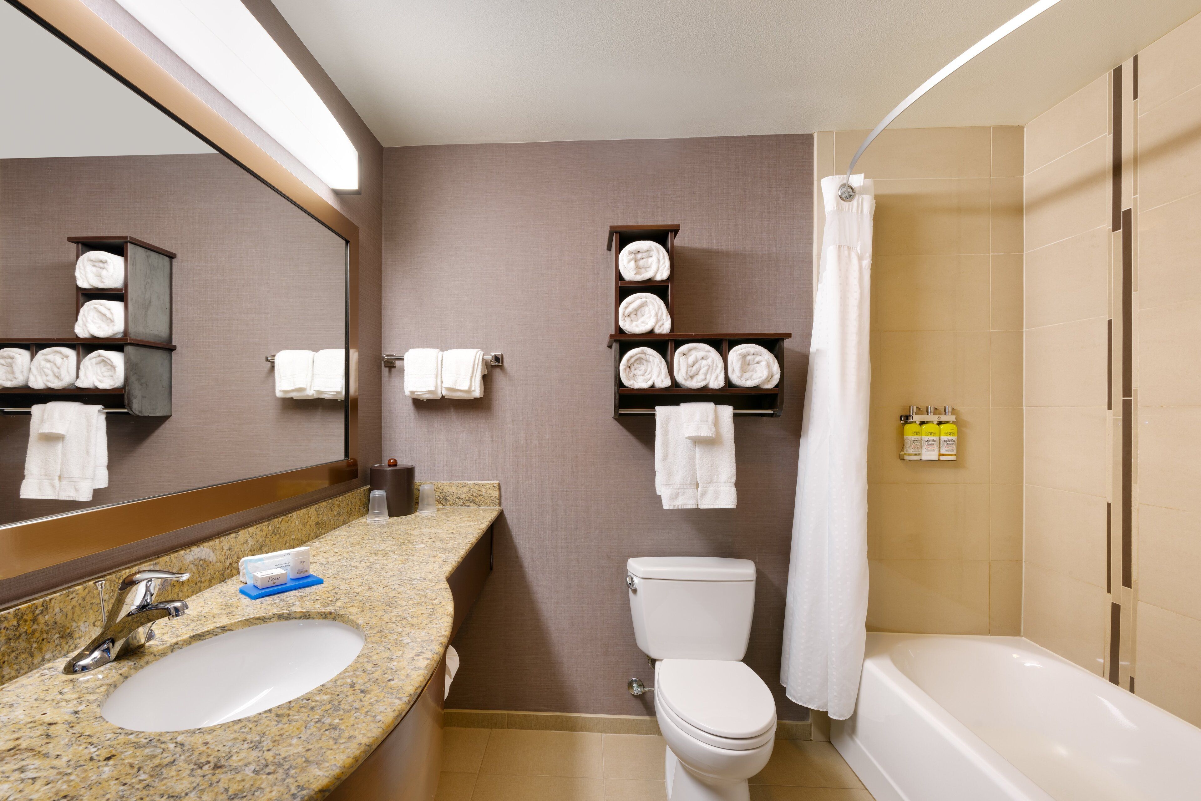 A bathroom with a granite sink, a toilet, a bathtub, and shelves with towels.