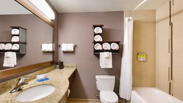 A bathroom with a granite sink, a toilet, a bathtub, and shelves with towels.