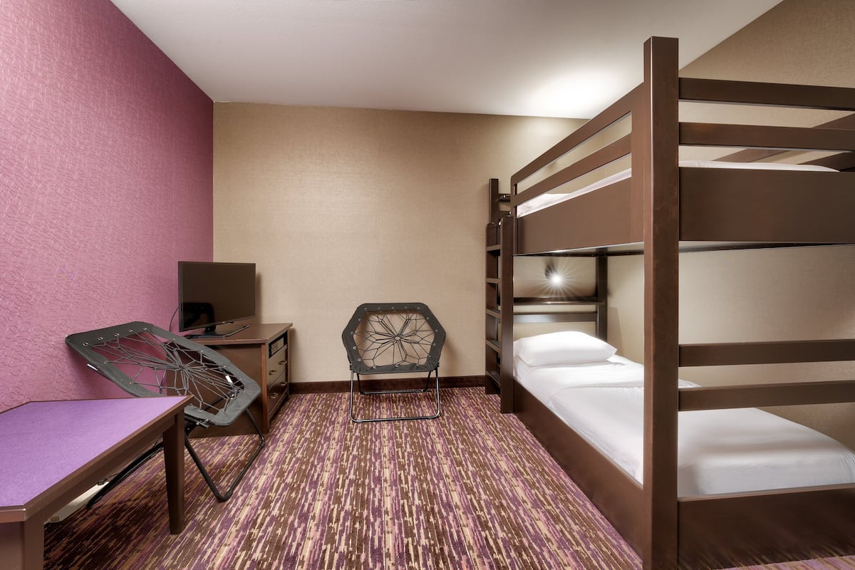 A compact hotel room with a bunk bed, a desk with a chair, a small table, and a television.