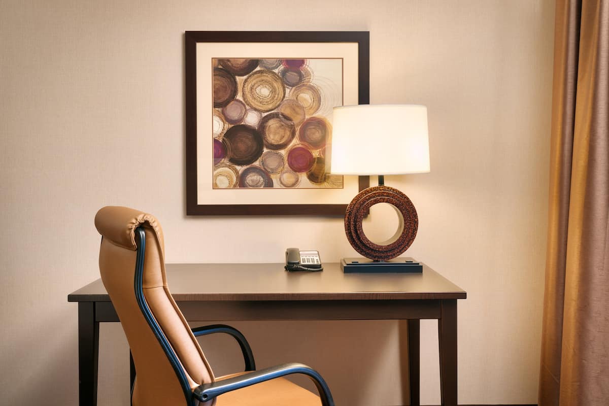 A chair with a headrest and armrests, a desk with a framed artwork, a lamp, and a telephone.