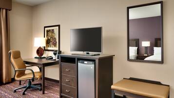 A hotel room with a desk, chair, television, and a bench.