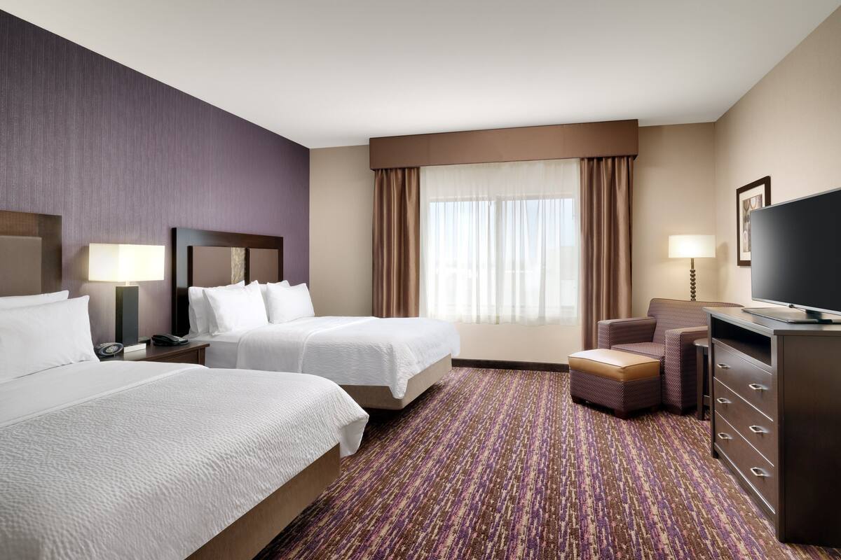 A hotel room with two beds, a sofa, a TV, and a desk.