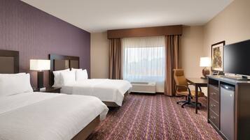 A hotel room with two beds, a desk, a chair, a television, and a window with curtains.