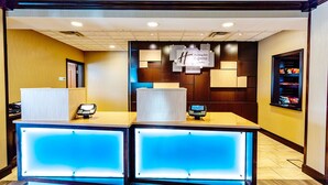 Modernilla designilla varustettu vastaanottotiski, jossa on sininen, valaistu paneeli ja sen yläpuolella oleva kyltti, josta ilmenee, että kyseessä on Holiday Inn Express Suites -hotelli.