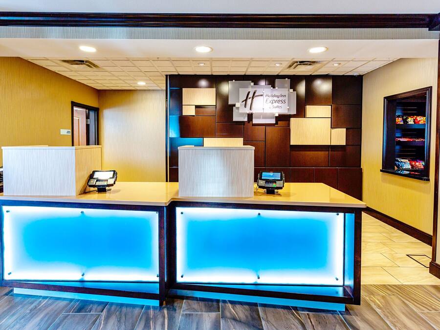 A reception desk with a modern design, featuring a blue illuminated panel and a sign above indicating it's a Holiday Inn Express Suites location.