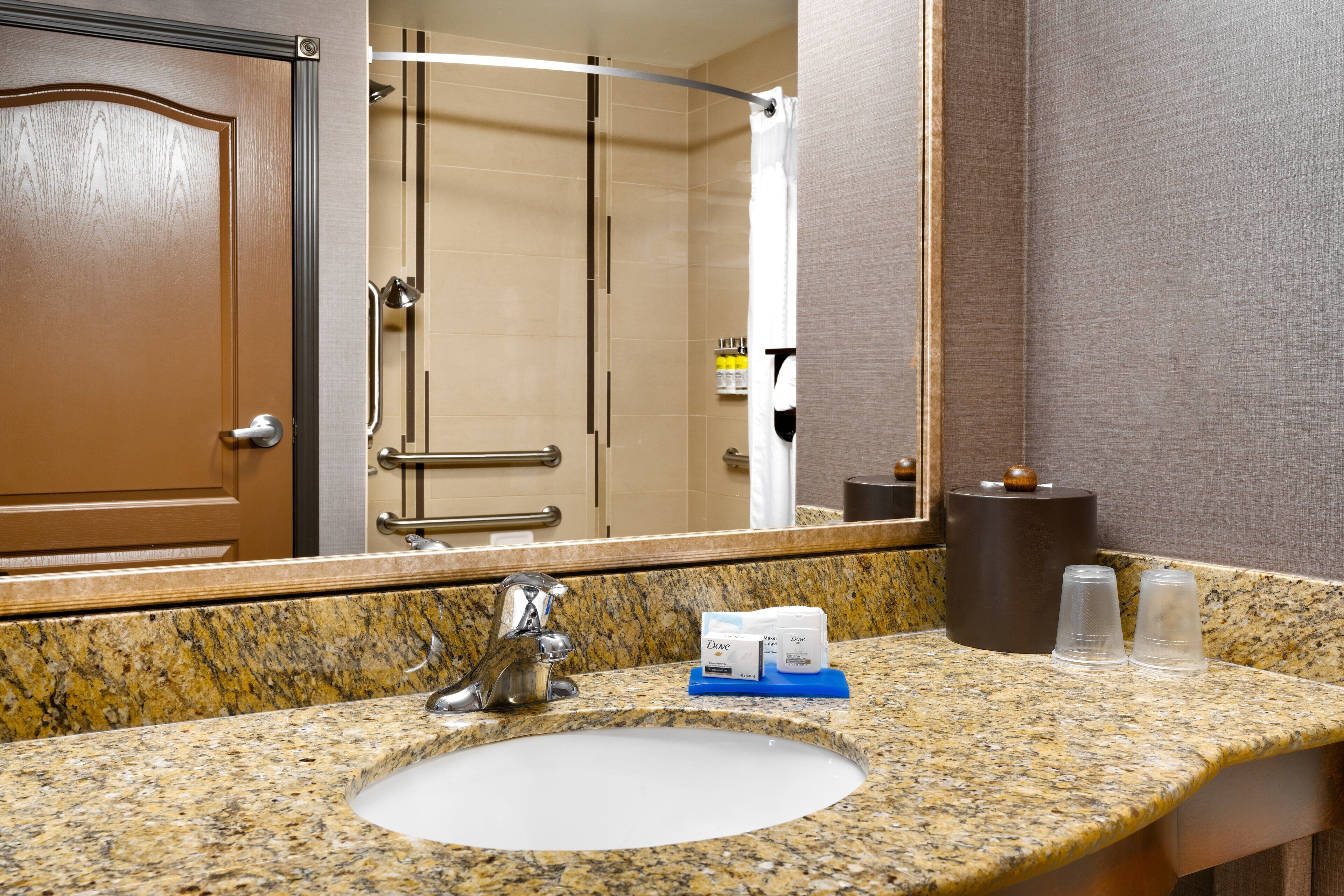 A bathroom with a granite countertop, a sink, a mirror, and a shower area.