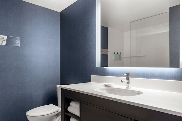 Et moderne badeværelse med en hvid vask, mørkt toiletbord og et stort spejl.
