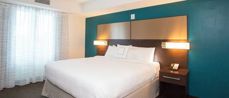 A hotel room with a large bed, two bedside tables, a telephone, and a window with curtains.