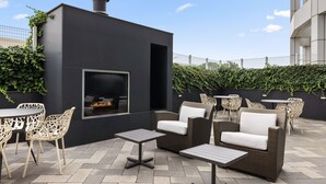 An outdoor patio with a modern fireplace, wicker furniture, and a view of the city skyline. - Residence Inn New York The Bronx At Metro Center Atrium (Bronx)