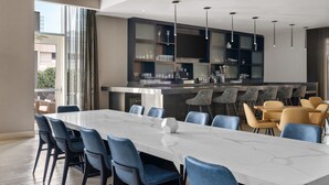 A modern dining area with a marble table and blue chairs, a bar area with stools, and a kitchen with dark cabinets and glassware. - Residence Inn New York The Bronx At Metro Center Atrium (Bronx)