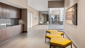 A modern kitchen with wooden cabinets, a stainless steel sink, and a long countertop. There are two yellow cushioned seating areas in the hallway. - Residence Inn New York The Bronx At Metro Center Atrium (Bronx)