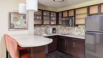 A modern kitchen with dark wood cabinets, a stainless steel refrigerator, a microwave, and a coffee maker.