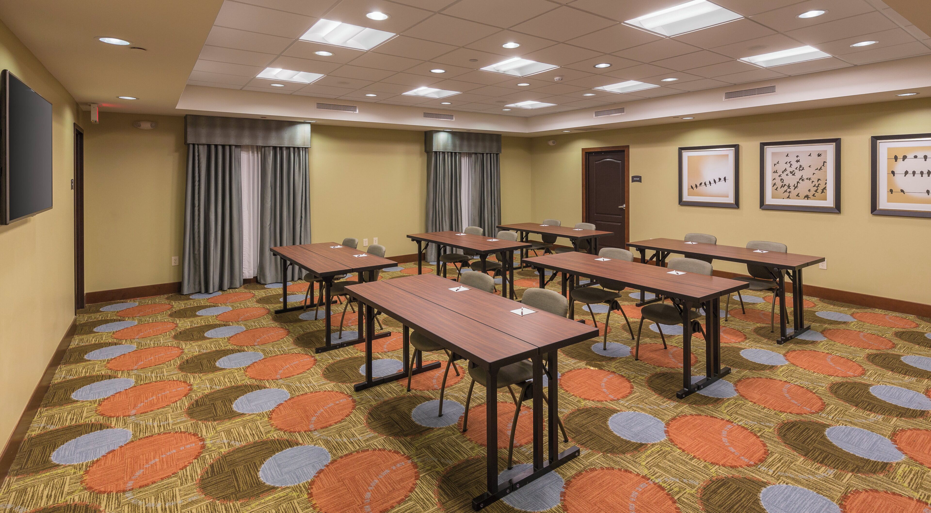 Une salle de conférence dotée de plusieurs tables et chaises, d’un tapis à motifs et de luminaires au plafond.