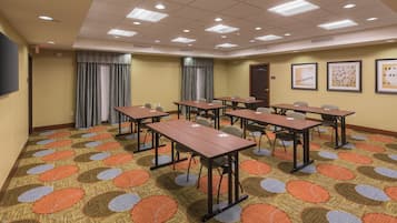 Une salle de conférence dotée de plusieurs tables et chaises, d’un tapis à motifs et de luminaires au plafond.