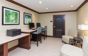 Habitación de hotel con un escritorio, dos monitores, una impresora, una silla, un sofá, una lámpara y dos cuadros en la pared.