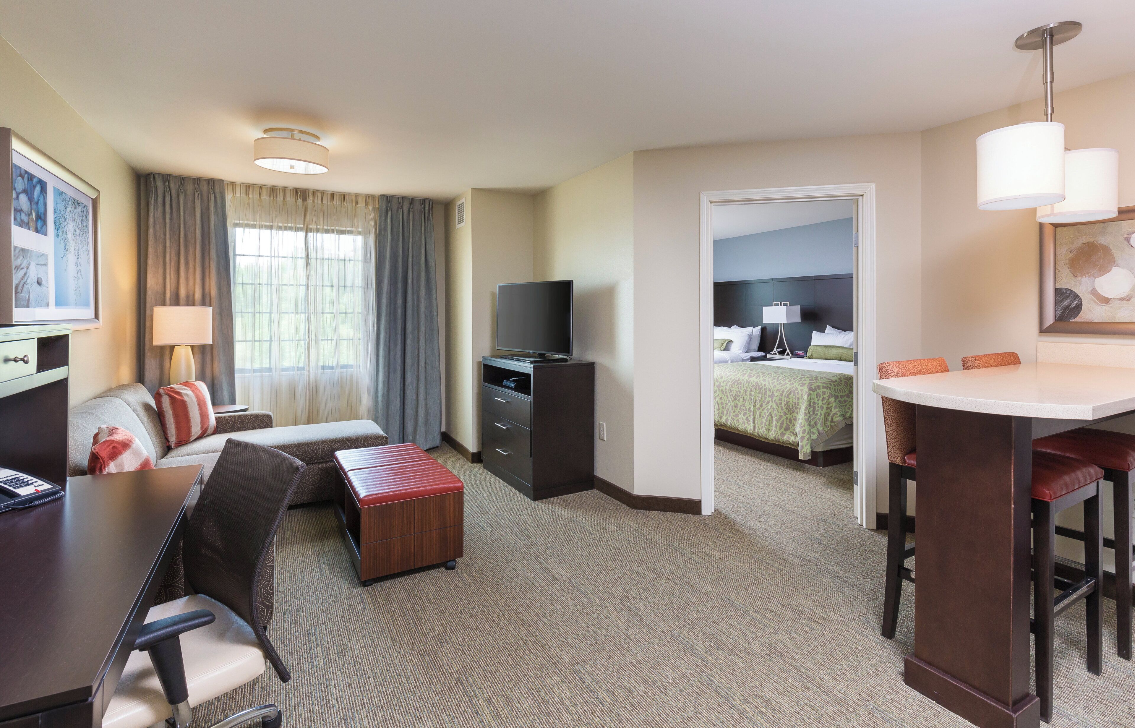 Habitación de hotel con sofá, televisor, escritorio, silla, mesita y cama con cubrecama verde.