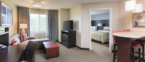 A hotel room with a sofa, a TV, a desk, a chair, a small table, and a bed with a green bedspread.