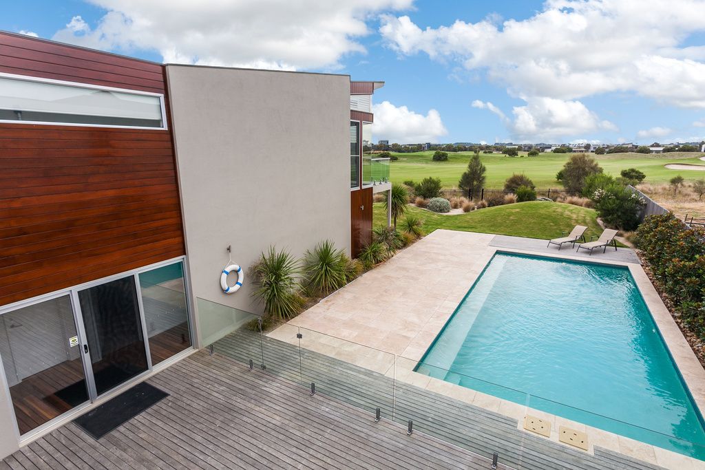 A modern building with a swimming pool, wooden deck, and a view of a golf course.