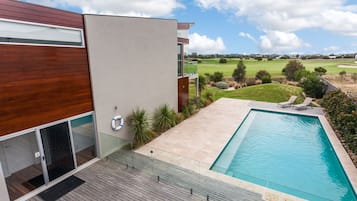 En modern byggnad med en swimmingpool, ett trädäck och utsikt över en golfbana.