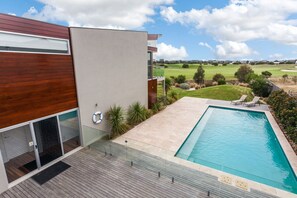Un bâtiment moderne doté d’une piscine, d’une terrasse en bois et offrant une vue sur un terrain de golf.