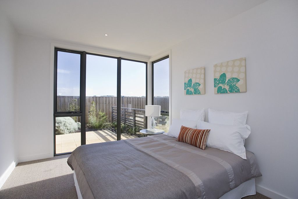 A bedroom with a large bed, a view through a sliding door to an outdoor area, and two wall-mounted artworks.