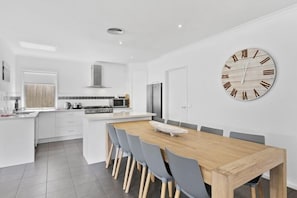 Une cuisine moderne avec des meubles blancs, une table à manger en bois et une grande horloge murale.