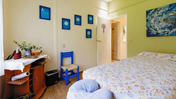 A bedroom with a bed, a chair, a desk, and a wall with framed pictures. - Agua Blanca (Jungapeo)