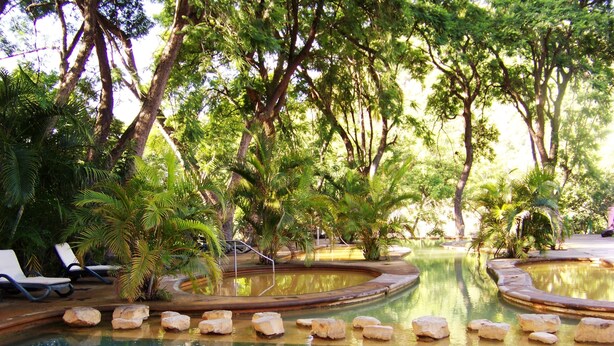 A pool area with lounge chairs and a circular water feature surrounded by trees. - Agua Blanca (Jungapeo)