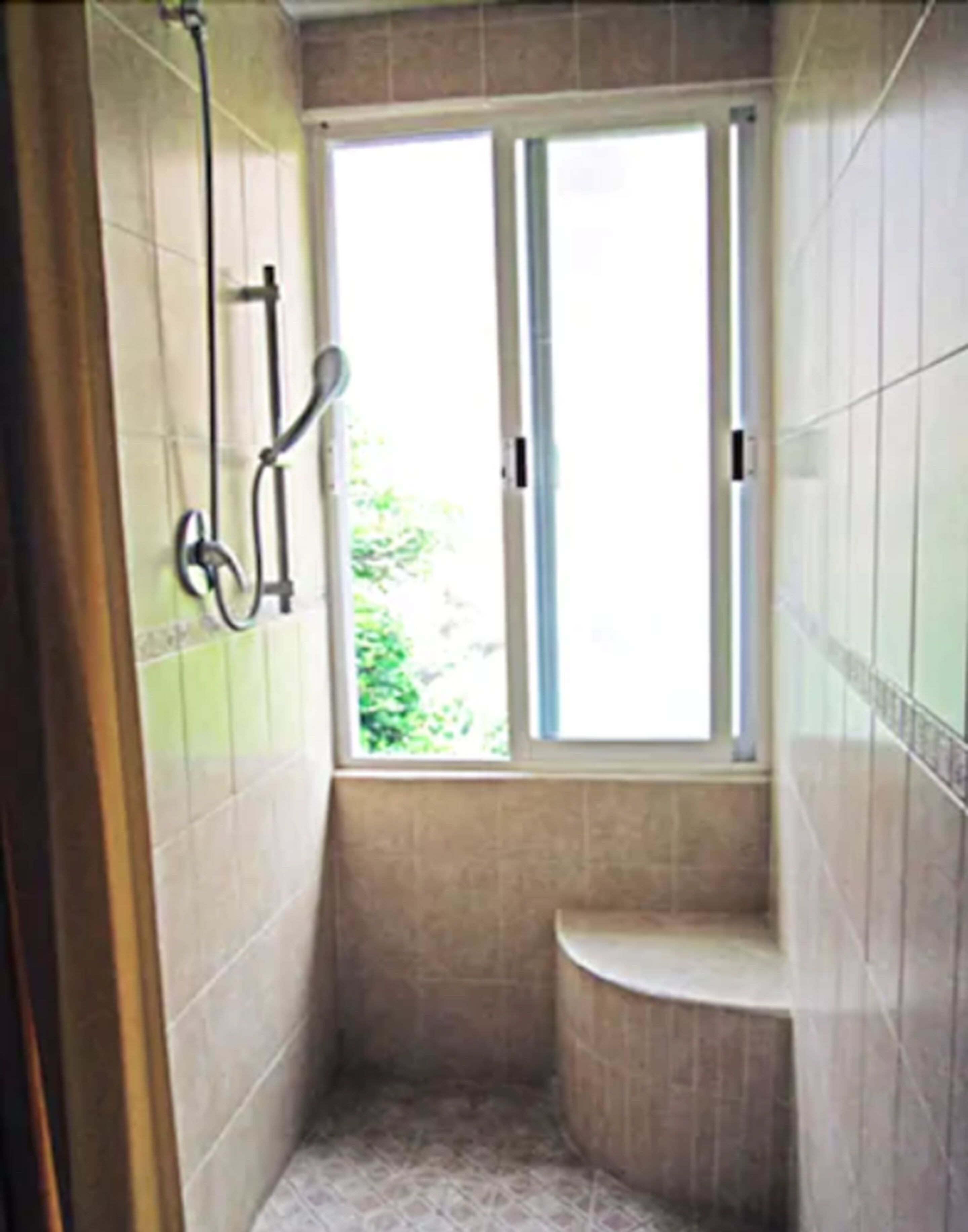 A small, tiled bathroom with a window, a shower, and a toilet.